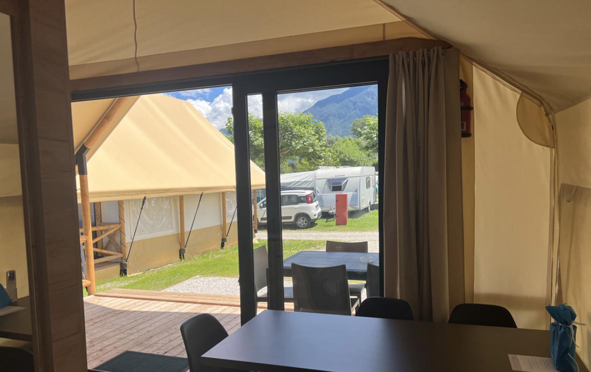 Binnen in een glamping tent met uitzicht op camping en bergen.