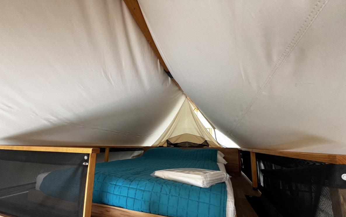 Binnenkant van een tent met tweepersoonsbed en blauwe deken.