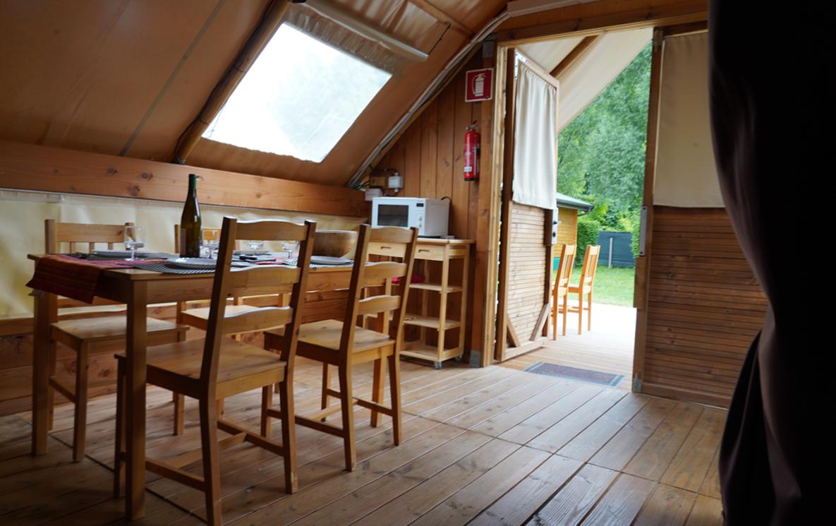 Interno di una tenda glamping con tavolo e sedie in legno.