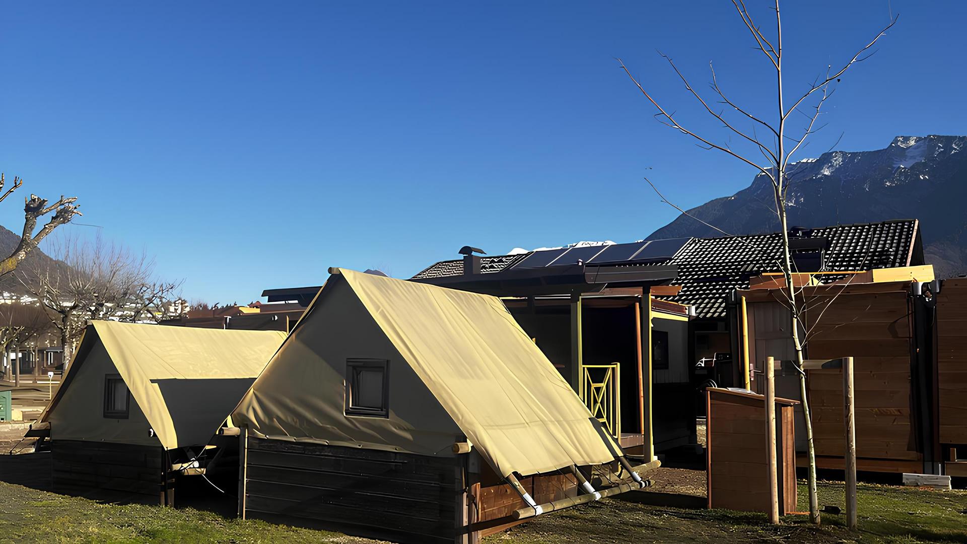 Glamping tents with colorful loungers in a sunny campsite.